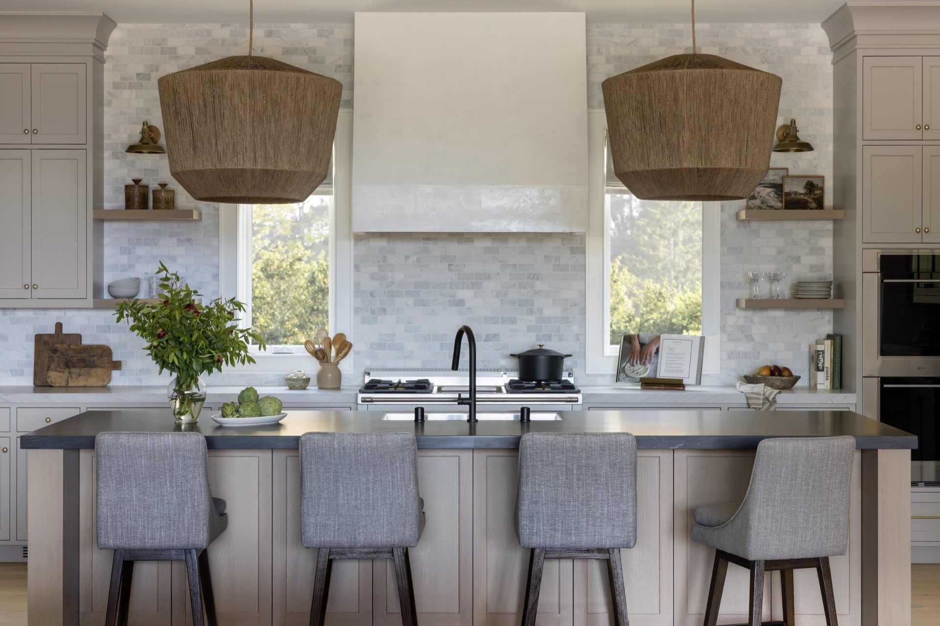A custom kitchen by The Builders Collective with marble backsplash, woven pendants, and a dark stone island.