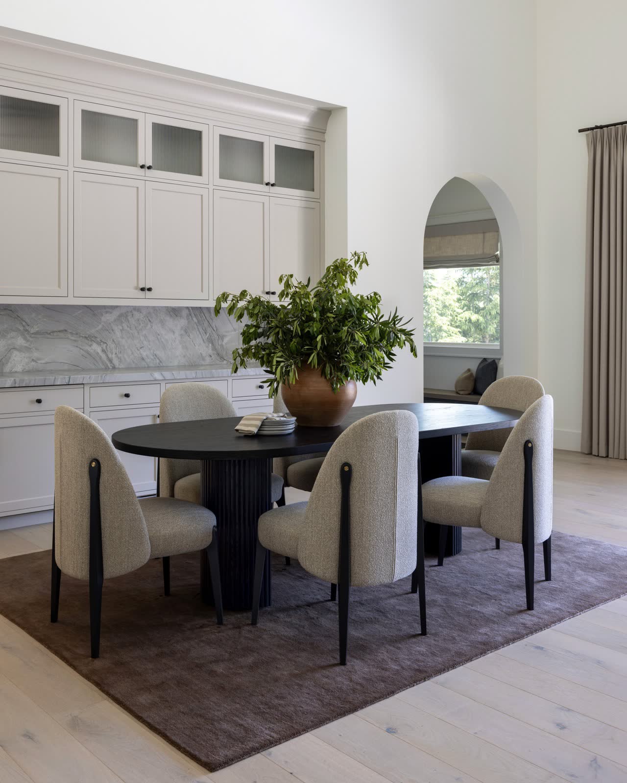 Dining room with a black oval pedestal table and cream chairs.