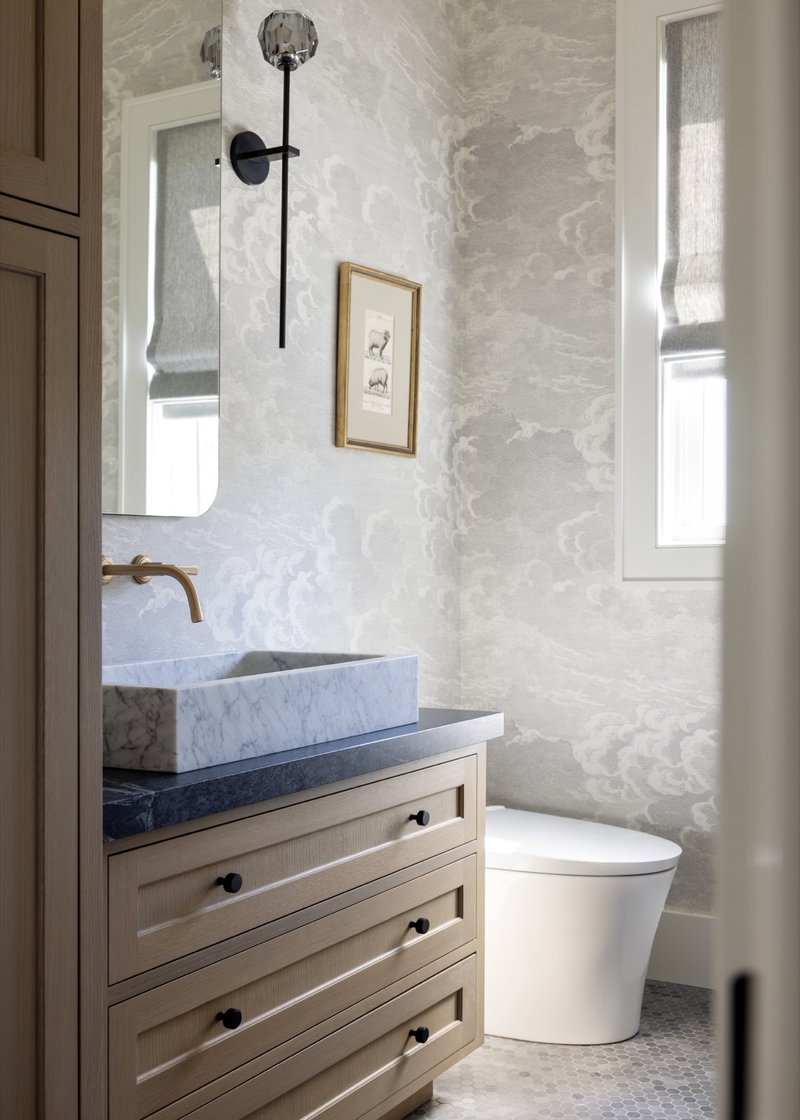 The powder room, cloud-patterned wallpaper and a carved marble vessel sink on an oak vanity.