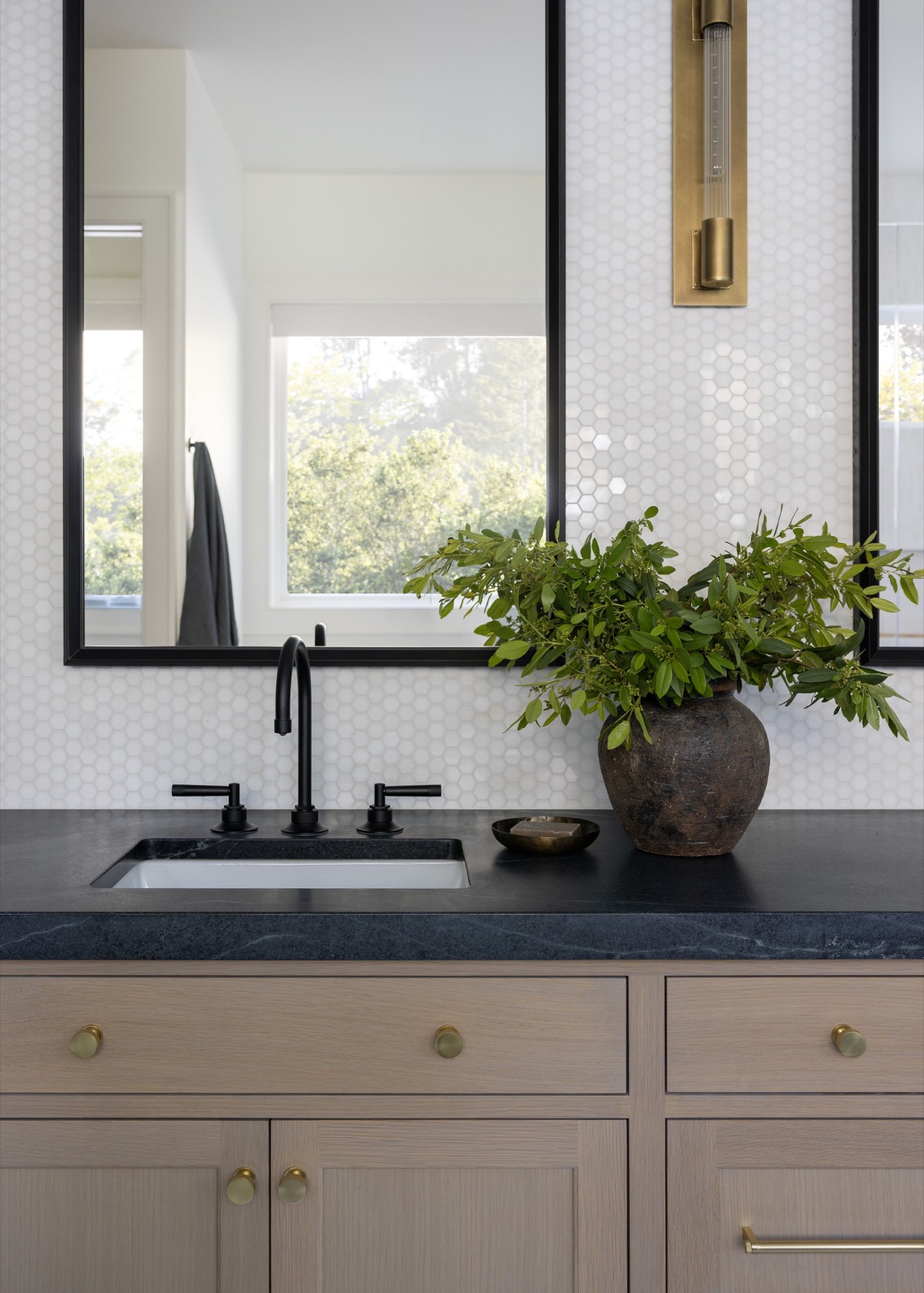 Vanity detail, black-framed mirror and brass sconce.
